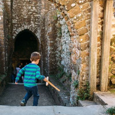 A young child running through archway at Mont Orgueil Castle with a wooden sword