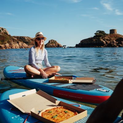 Couple sitting on paddle boards in the sea eating pizza