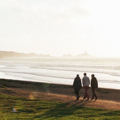 three people walking along coast near beach and rolling waves