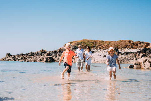 Two children and parents at beach paddling in clear shallow water