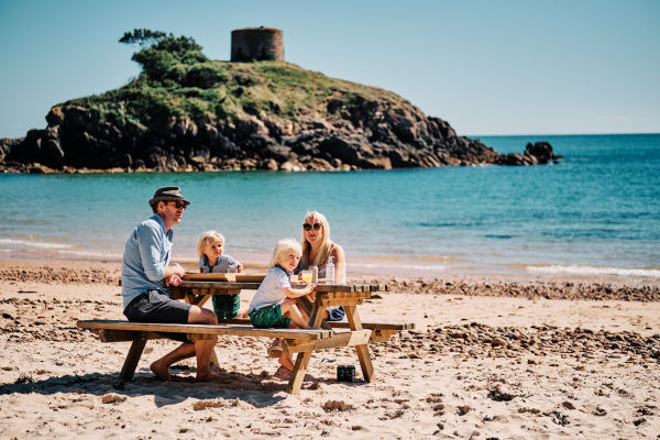 A family sitting at a picnic table on the sand atPortelet Bay.