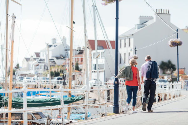 A couple walk along the harbour in St. Aubin