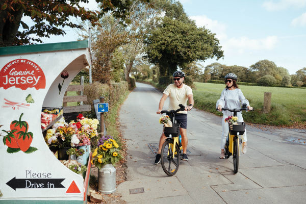 A couple on e-bikes stopping at a farm stall in Jersey