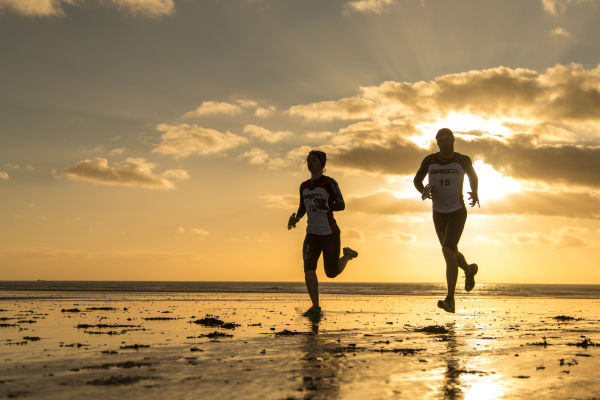 Two athletes running along the beach at sunrise