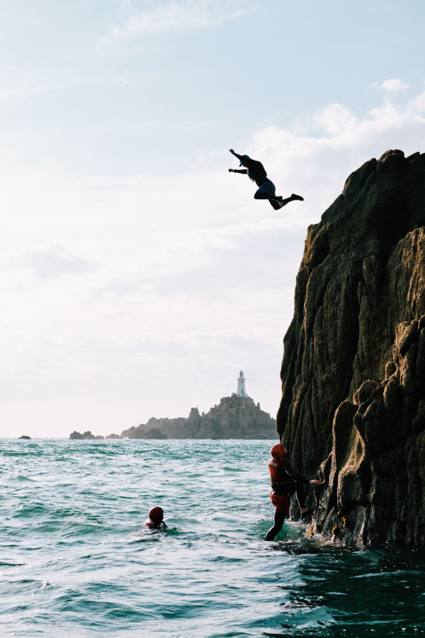 Person jumping off rock face into the sea by by Corbiere