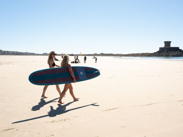 Two ladies walking along St. Ouen’s Bay with a stand up paddle board