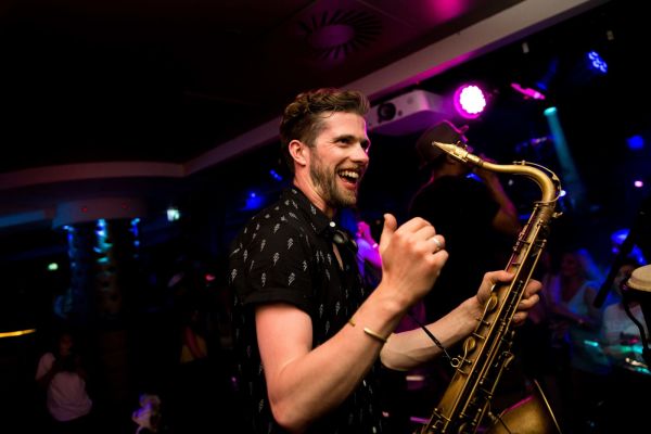 A smiling musician holding a saxaphone in a nightclub.