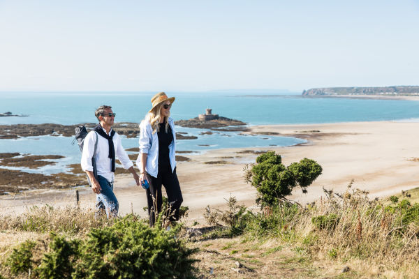 Couple walking on a headland with the sea and the beach behind them