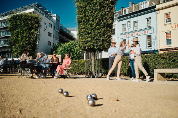 Group of people in a town square playing Petanque and having drinks