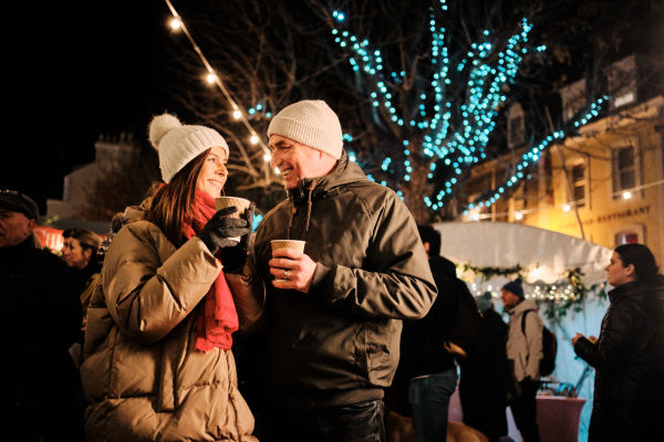 Couple at a Christmas market in front of a tree with fairy lights