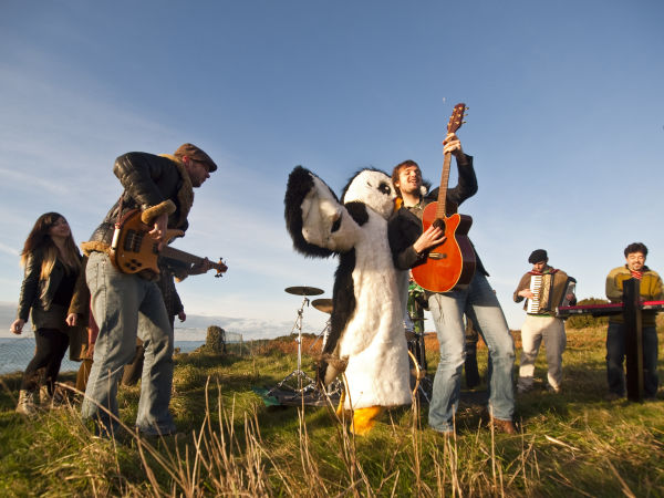A picture of Badlabecques playing on the North Coast with someone dressed as a puffin with them.