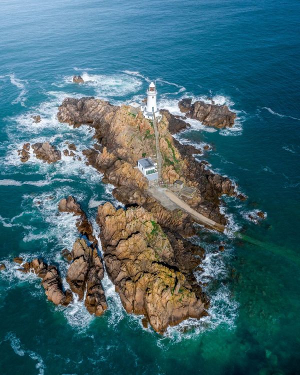Aerial shot of a lighthouse sitting on top of a rocky outcrop