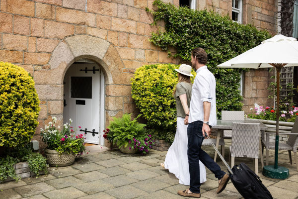 Stylish couple walking into a charming countryside hotel with a small suitcase