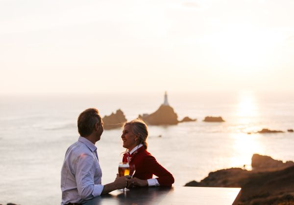 A couple having a drink with La Corbière Lighthouse in the background