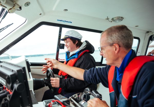 A boy with downs syndrome behind the wheel of a boat on a Wet Wheels tour with the captain