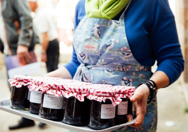 A woman holding jars of Jersey Black butter. The seal has been decorated with a pink and white checked piece of a fabric covering it.