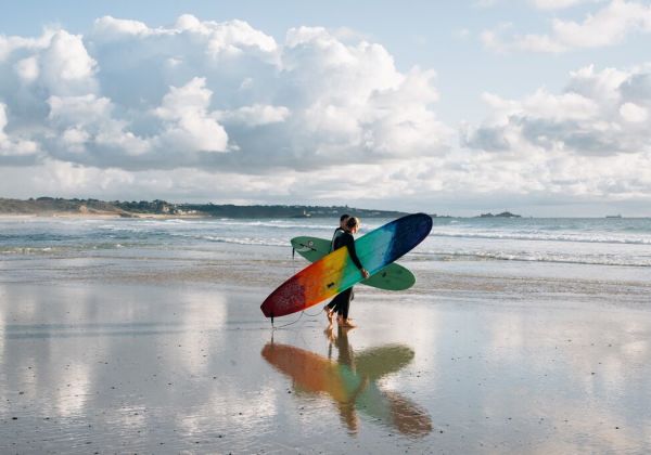 Two surfers with colourful boards walking towards the sea on St. Ouen