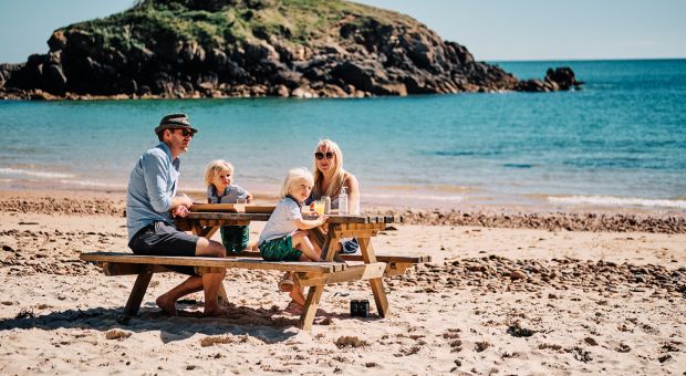 A family sitting at a picnic table on the sand atPortelet Bay.