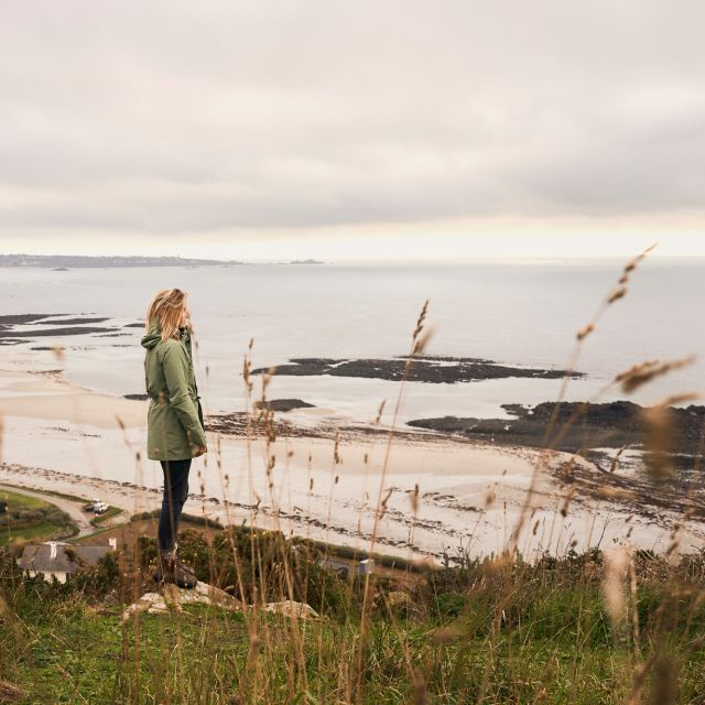 Woman staning on a clifftop taking in the view of a sandy beach